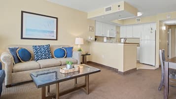 A living room with a sofa, coffee table, and a kitchen area with cabinets and appliances.