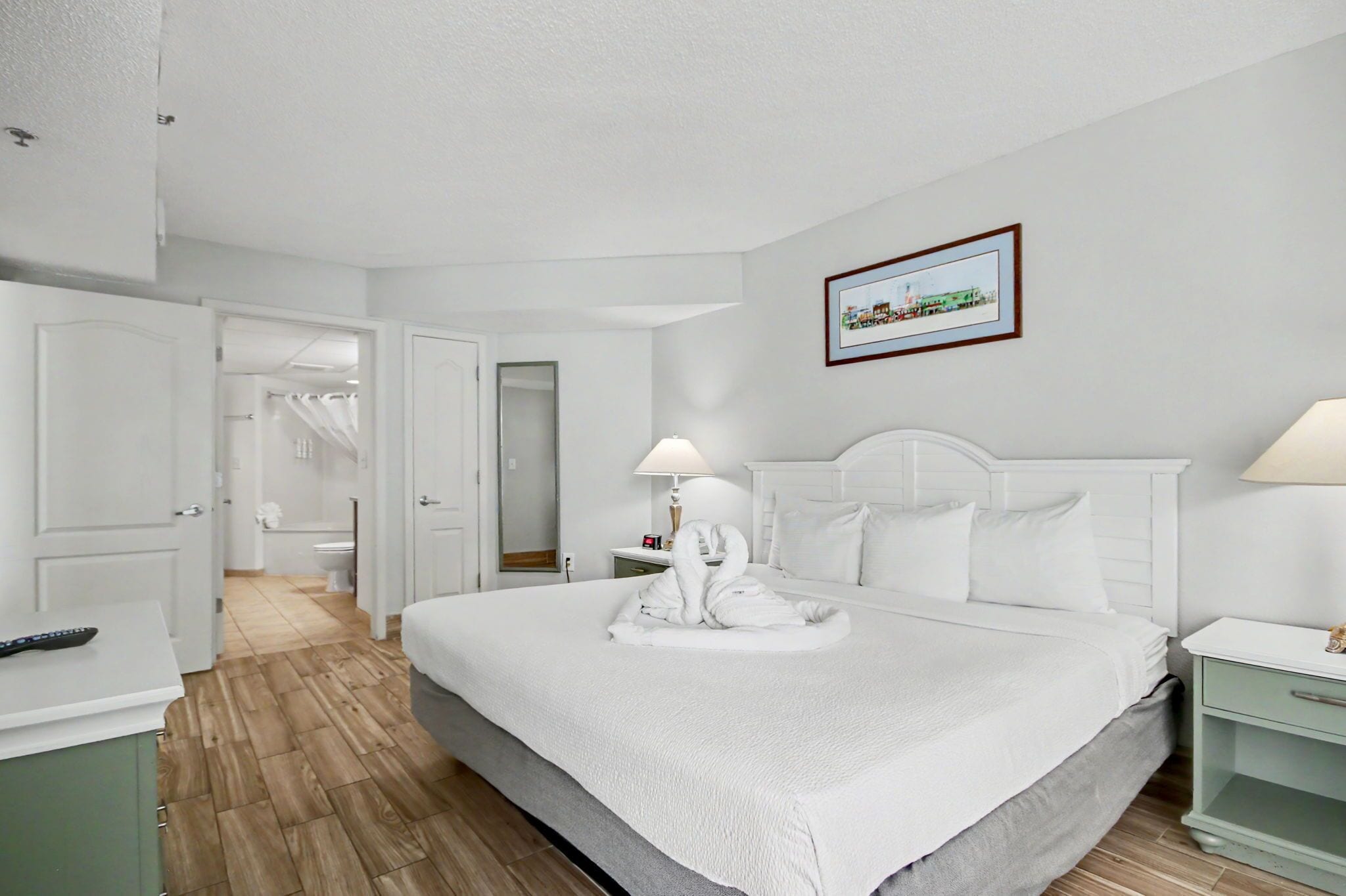 Habitación de hotel con una cama grande, una mesita de noche, un espejo y un cuadro en la pared.