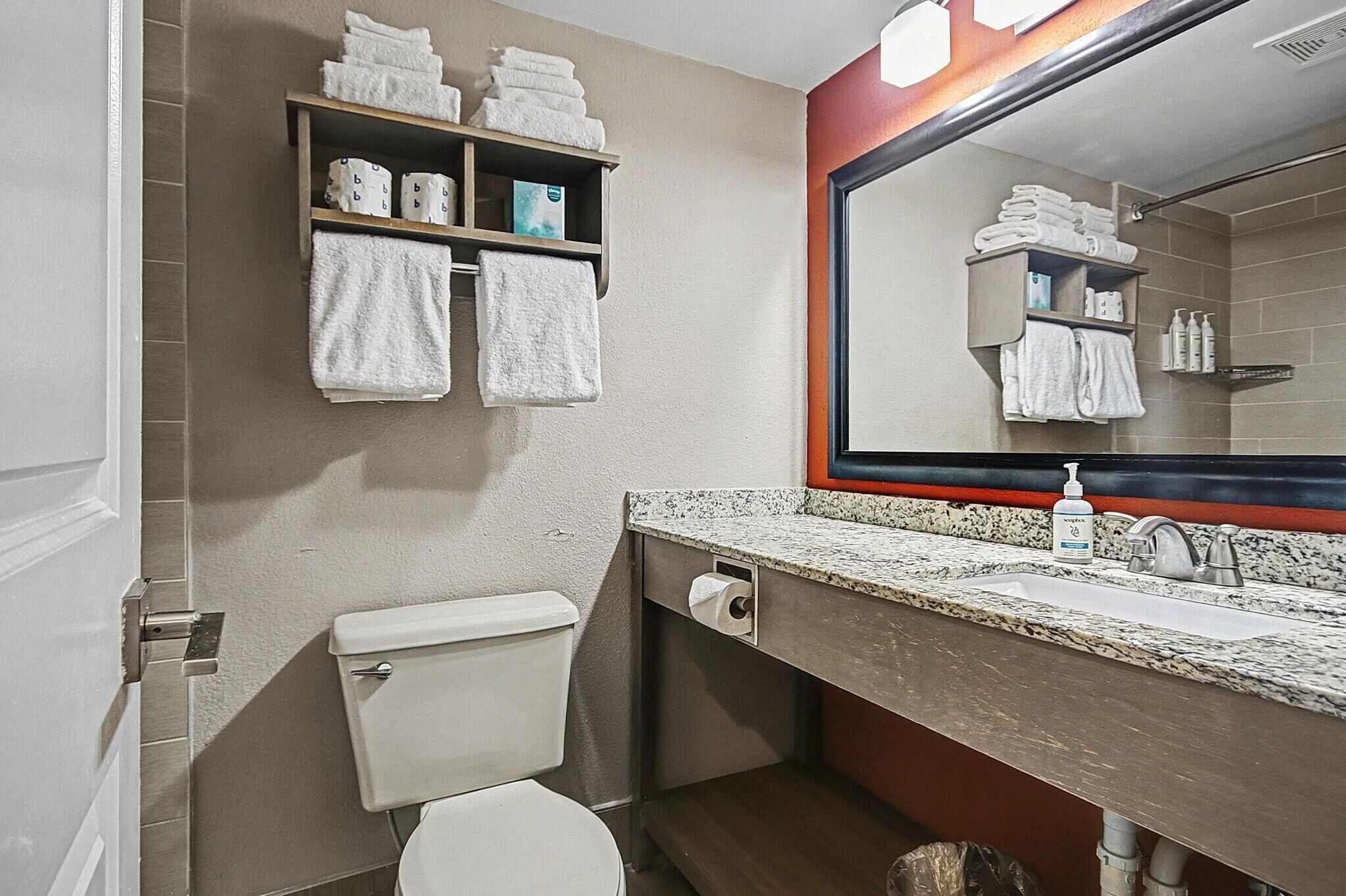 A bathroom with a toilet, sink, mirror, towel rack, and shelves with towels and toiletries.