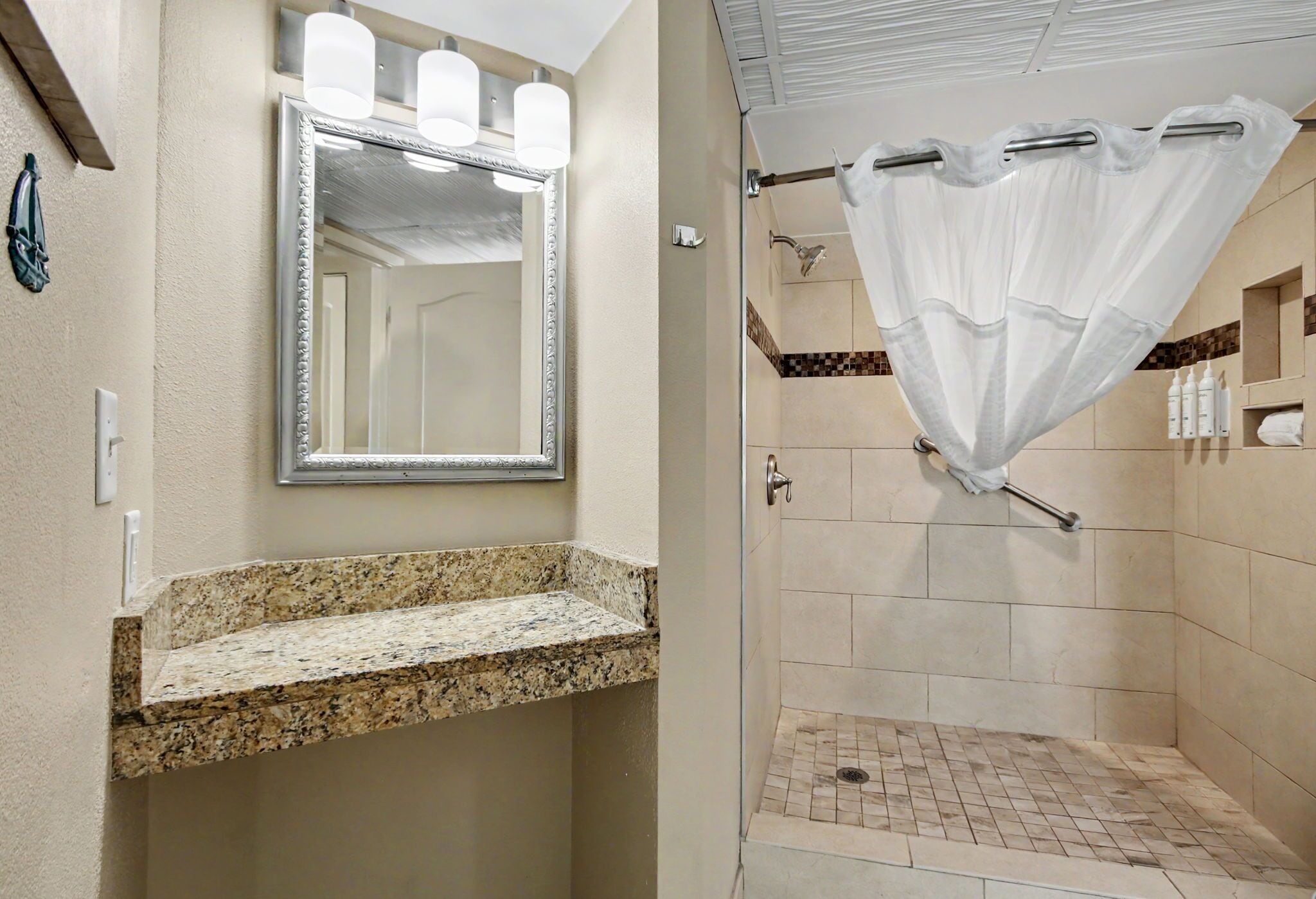 A bathroom with a granite countertop, a mirror, a shower with a curtain, and tiled walls.
