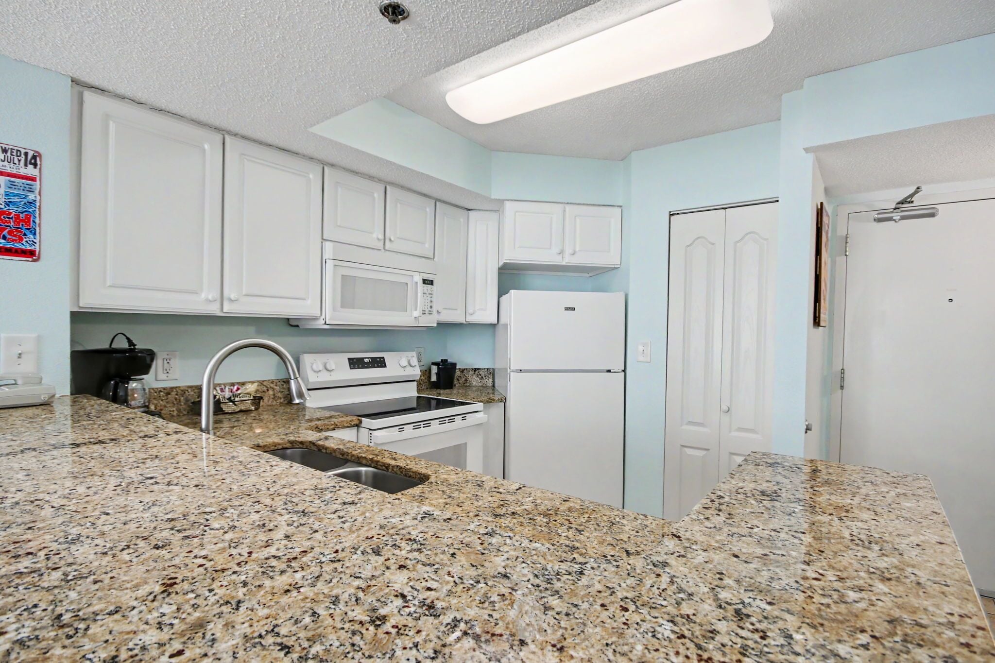 A kitchen with granite countertops, white cabinets, a microwave, stove, refrigerator, and a sink.