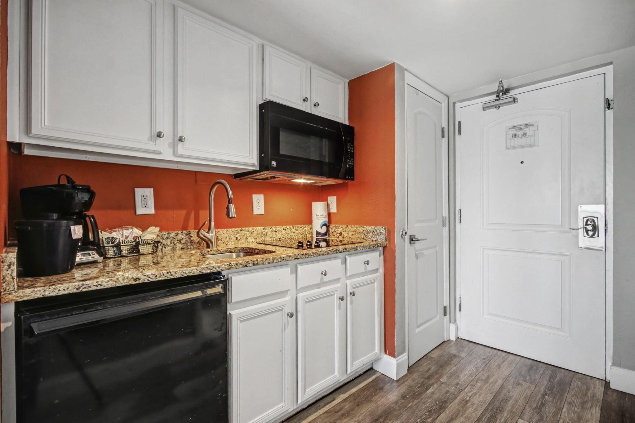 A kitchen with white cabinets, a black microwave, a granite countertop, and a dishwasher.