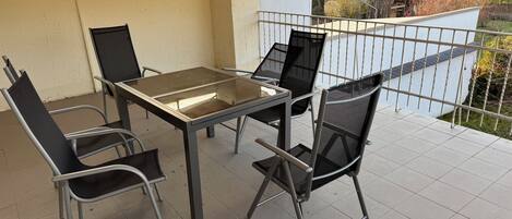 En overdækket terrasse med et bord og fire stole.