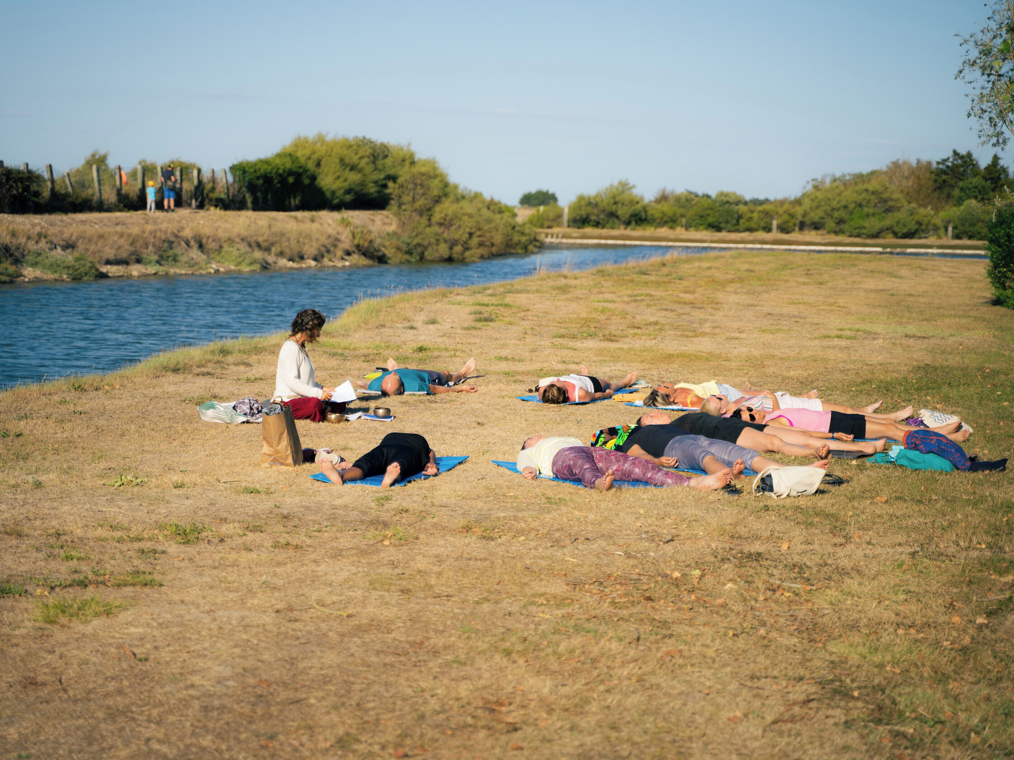 A group of people lying on mats in a grassy area near a body of water.