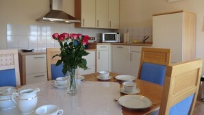 Uma sala de jantar com mesa posta para quatro pessoas, um vaso com flores e um micro-ondas ao fundo.