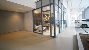Un bâtiment moderne doté d’une façade en verre, d’un espace d’accueil avec des sièges et d’un parking avec des voitures.