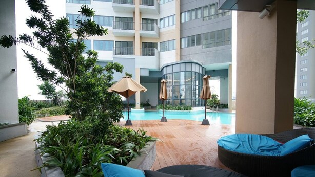 Un espace piscine extérieur moderne, doté de chaises longues et de parasols, entouré de verdure et avec un immeuble à plusieurs étages en arrière-plan.