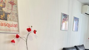 Een moderne woonkamer met een houten eettafel, zwarte stoelen, een zwarte leren bank en een vaas met rode bloemen aan de muur.