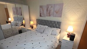Un dormitorio con una cama grande, un armario con espejo y una mesita de noche con lámpara.