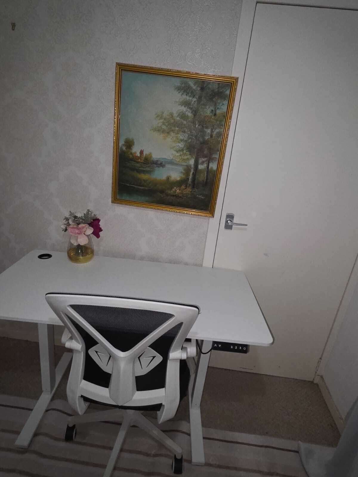 Una taula blanca amb una cadira, un quadre al mur i un vas petit amb flors sobre la taula.