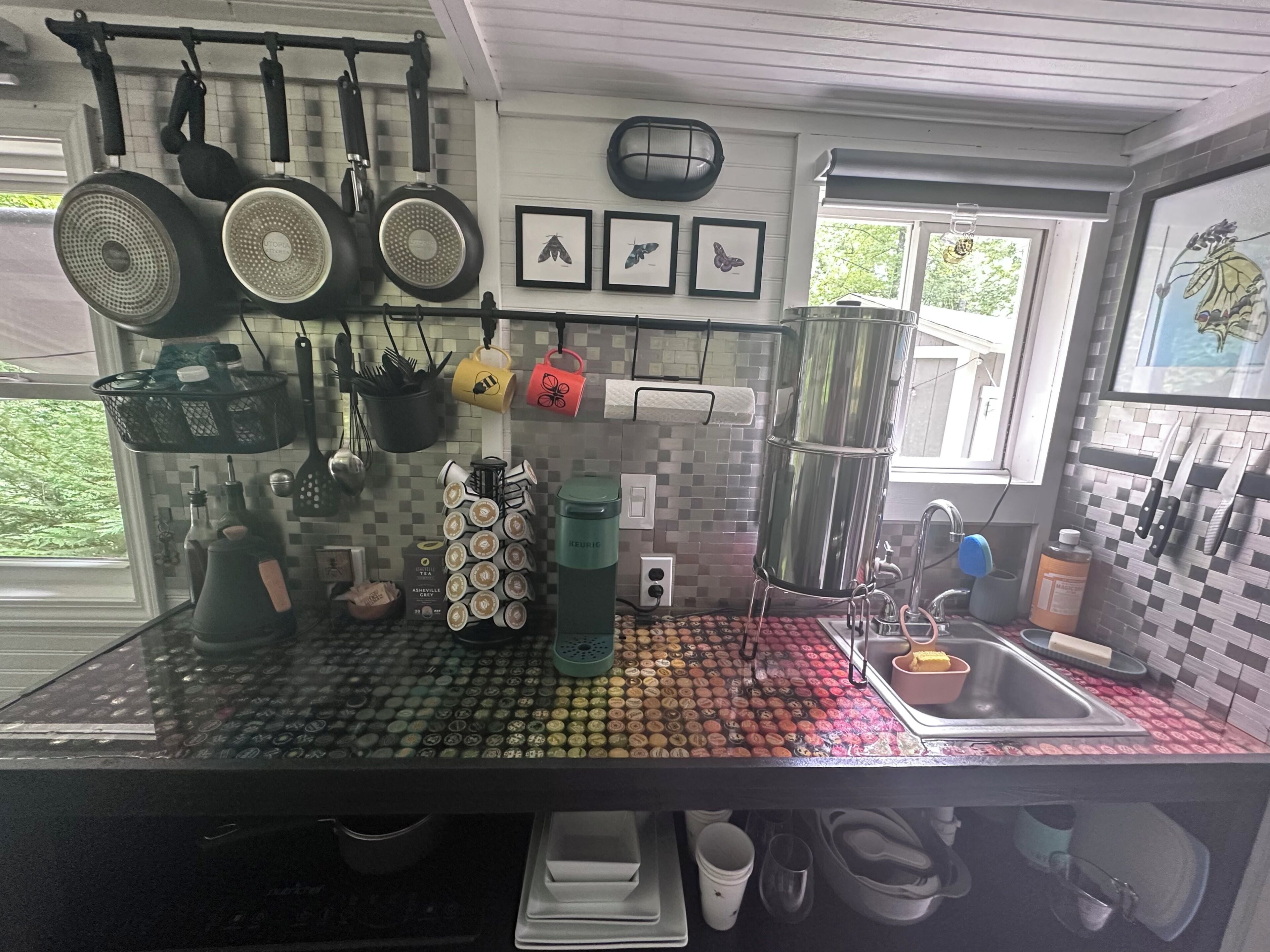 A kitchen with a tiled backsplash, hanging pots, a coffee machine, and a window with a view of greenery.