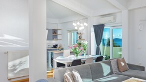 Ein modernes Wohnzimmer mit grauem Sofa, einem Esstisch mit Stühlen und einer Küche im Hintergrund.
