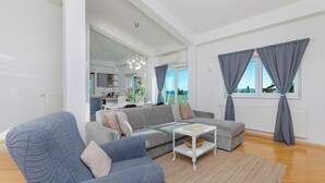 Ein modernes Wohnzimmer mit einem grauen Ecksofa, einem weißen Couchtisch und einem großen Fenster mit grauen Vorhängen.