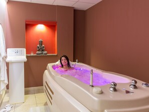 A person relaxing in a bathtub with a control panel and a statue on a shelf in the background. - CampingSpa - Confort 4 TV - 9p (5) (La Couarde-sur-Mer)