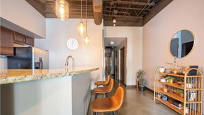 A modern kitchen with a bar area, wooden stools, a clock, and a mirror on the wall. - Sleek Industrial Loft in Short North Near OSU with King Beds & Fast WiFi (Columbus)
