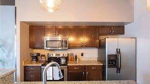 A modern kitchen with granite countertops, stainless steel appliances, and wooden cabinets. - Sleek Industrial Loft in Short North Near OSU with King Beds & Fast WiFi (Columbus)