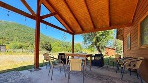 Un patio cubierto con techo de madera, mobiliario exterior y vistas a un paisaje montañoso.
