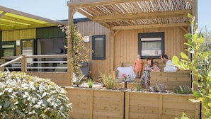 Un espace extérieur aménagé avec des sièges en bois et une pergola, entouré de plantes et d’une clôture en bois.
