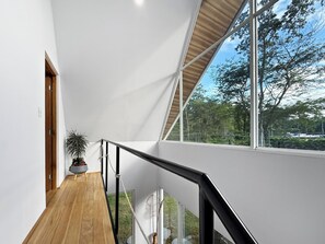 A modern interior with a wooden floor, white walls, and a large window offering a view of trees and a clear sky. - Crystal Jungle Villa - Brand new with AC, Laundry, Wifi (Puerto Viejo de Talamanca)