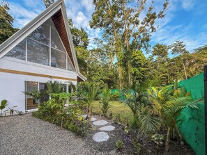 A modern house with a triangular roof, large windows, and a garden with a gravel path and tropical plants. - Crystal Jungle Villa - Brand new with AC, Laundry, Wifi (Puerto Viejo de Talamanca)