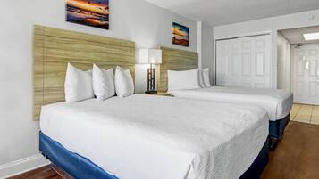 A hotel room with two beds, a wooden headboard, a nightstand, and a door.