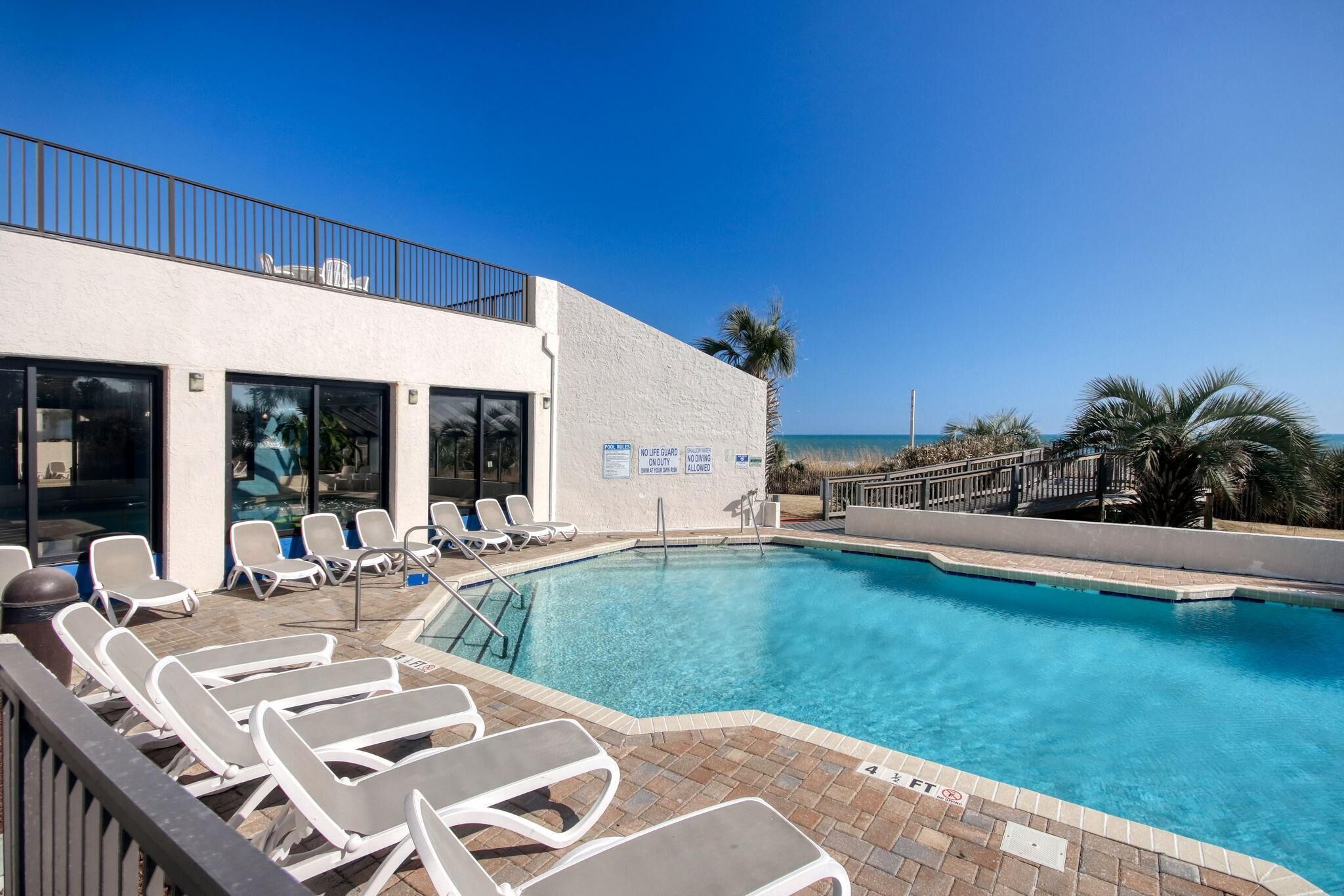 A pool area with lounge chairs, a lifeguard sign, and a view of the ocean.