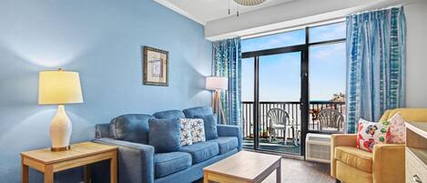 A living room with a blue sofa, a wooden coffee table, a yellow armchair, and a ceiling fan.