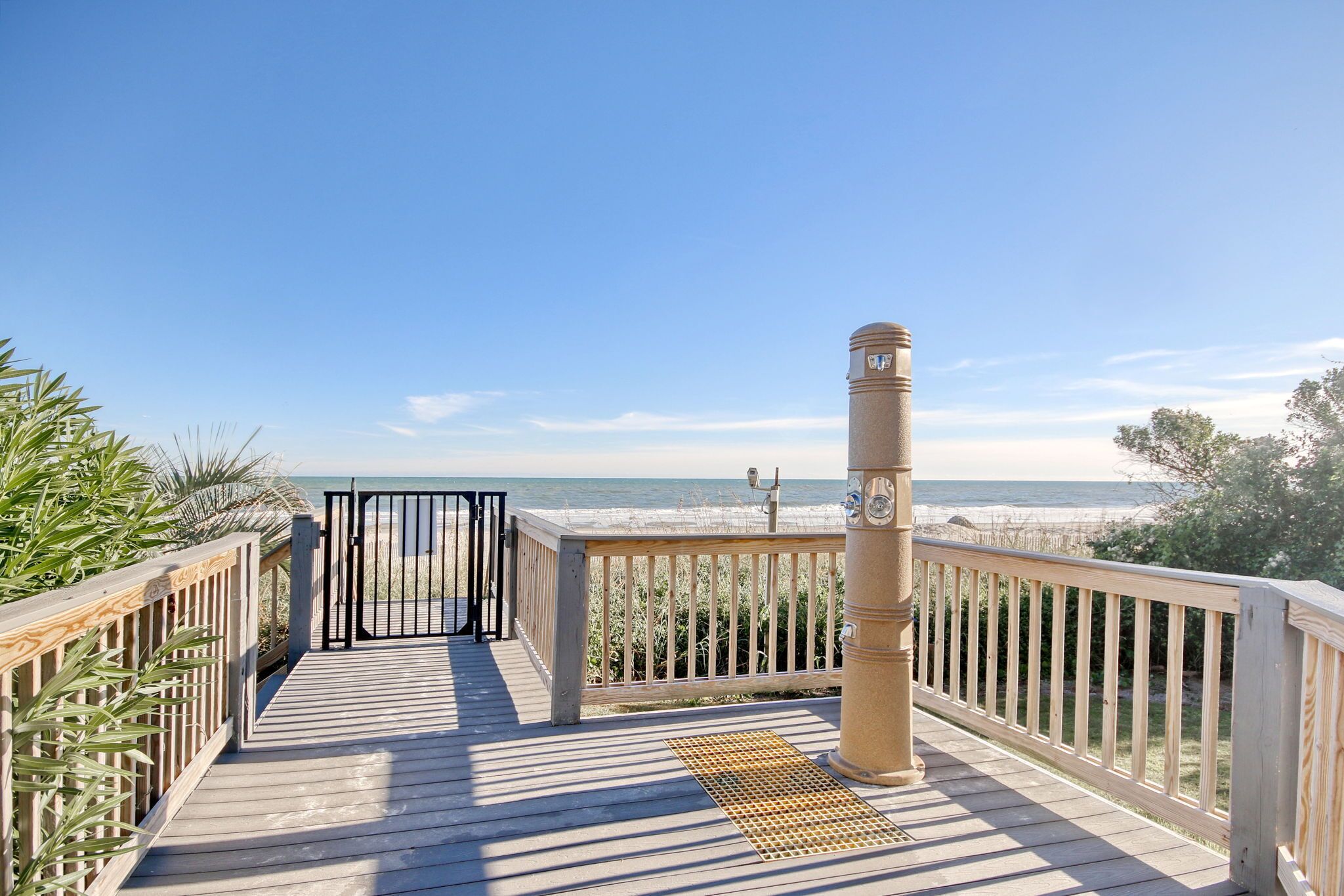 A wooden deck with a metal gate leading to a beach view.