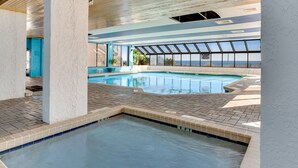 Une piscine dotée d’une terrasse carrelée et offrant une vue sur l’océan grâce à de grandes fenêtres.