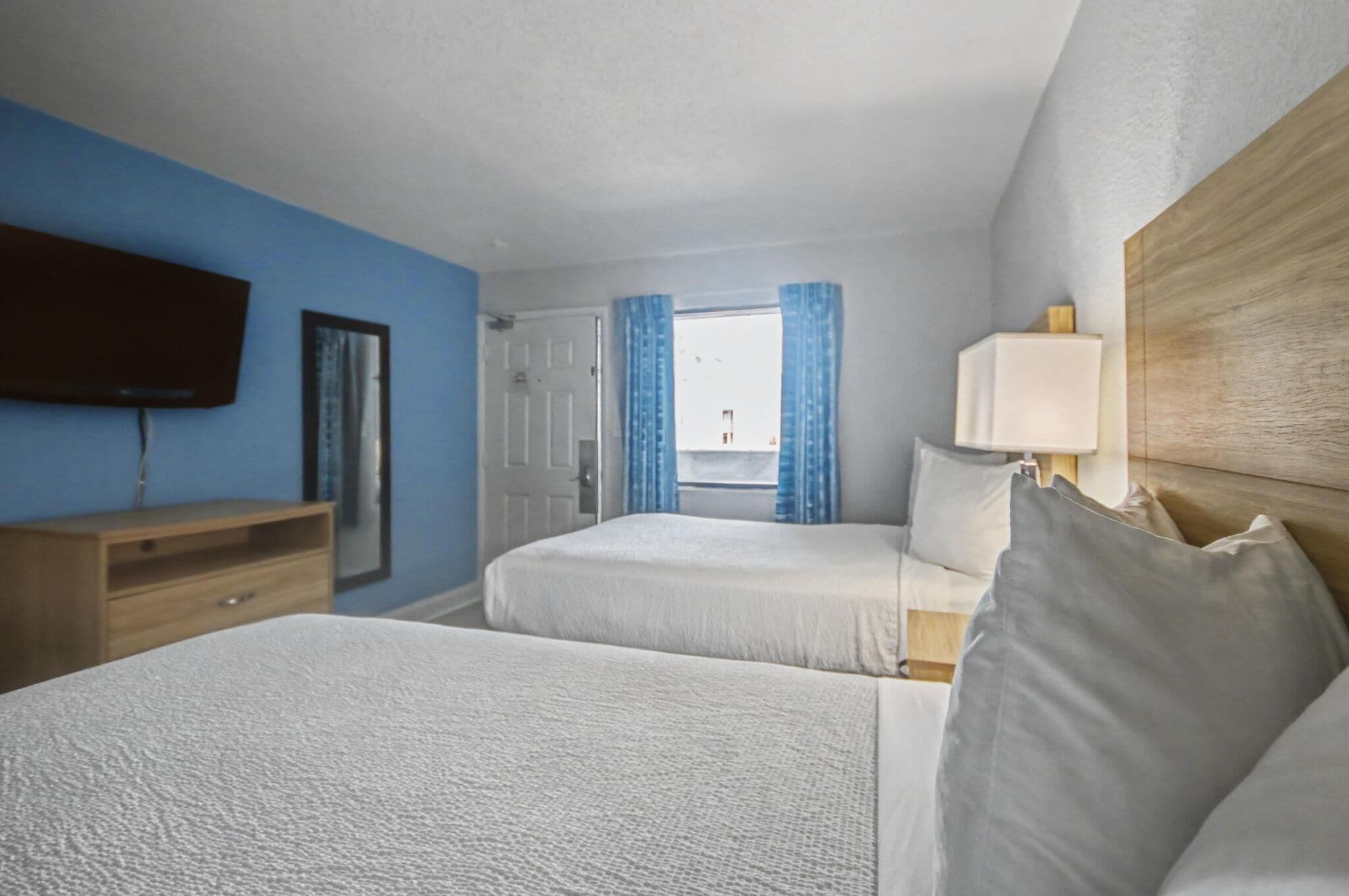 Habitación de hotel con dos camas, un televisor, un aparador de madera y una ventana con cortinas.