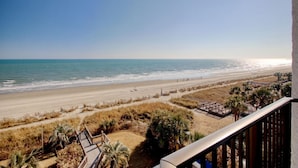 Une vue sur la plage depuis un balcon avec une terrasse en bois, une plage de sable et un ciel dégagé.