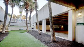 A courtyard with artificial grass, palm trees, and a covered area with a sign about dog walking regulations.