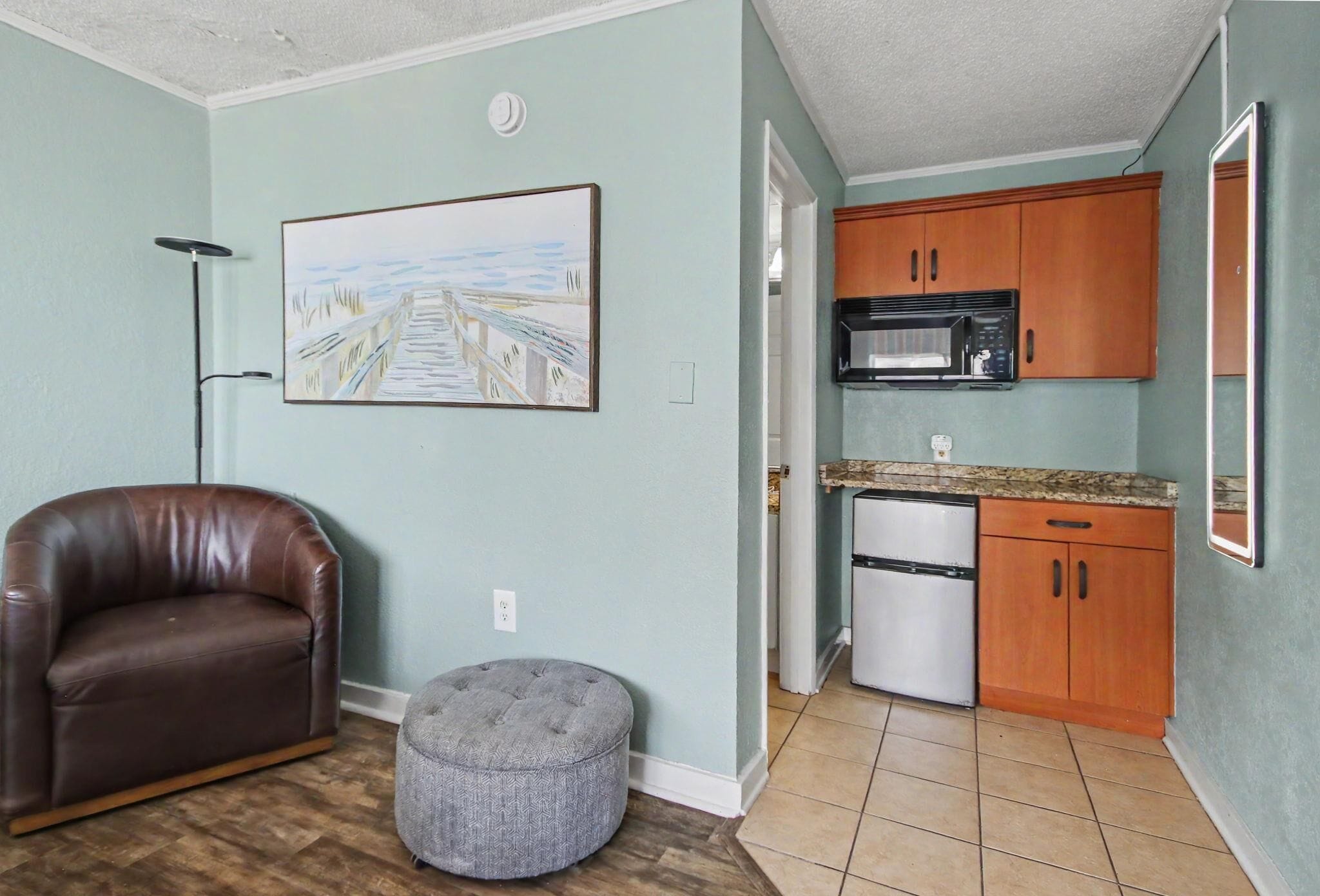 A living room with a brown leather sofa, a grey ottoman, and a painting of a bridge on the wall.