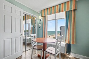 Une pièce avec une table et des chaises, une vue sur la plage et une porte donnant sur une autre pièce.