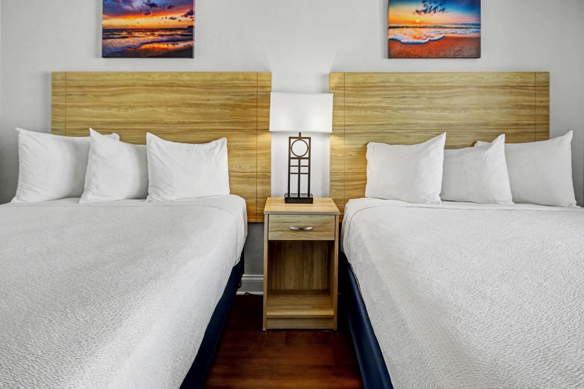 Une chambre d’hôtel avec deux lits, une table de chevet avec une lampe et des œuvres d’art accrochées aux murs.
