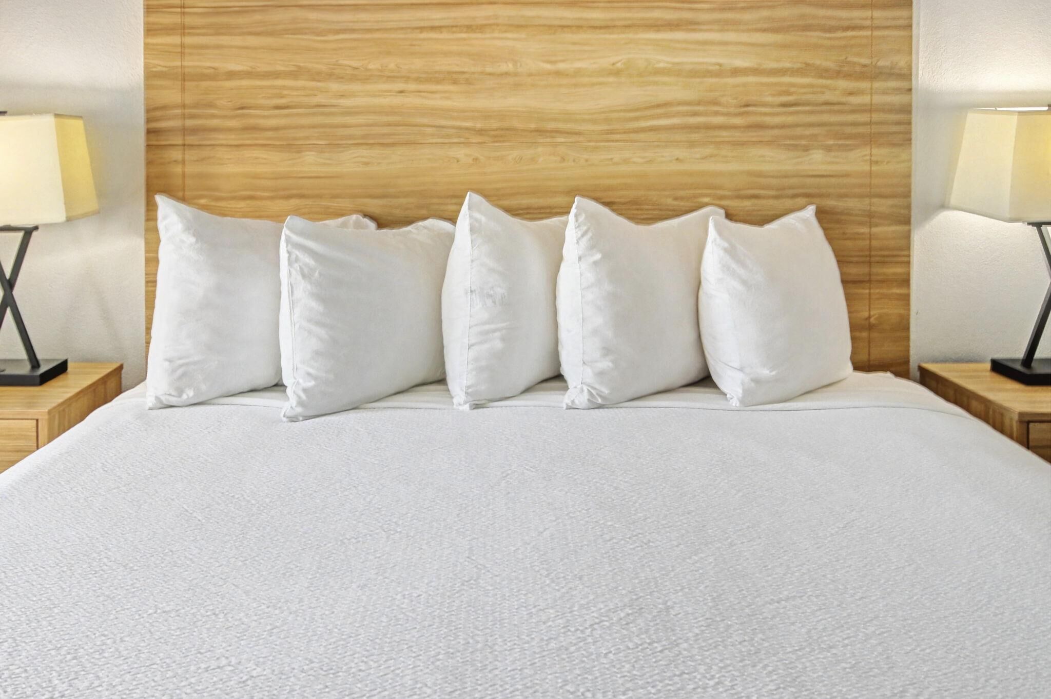 A neatly made bed with a wooden headboard, white bedding, and two bedside lamps on wooden nightstands.