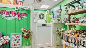 Un spa y refugio acogedor para mascotas, con una pared verde, un letrero que dice 'Merry and Bright' y varios productos para animales en estantes.