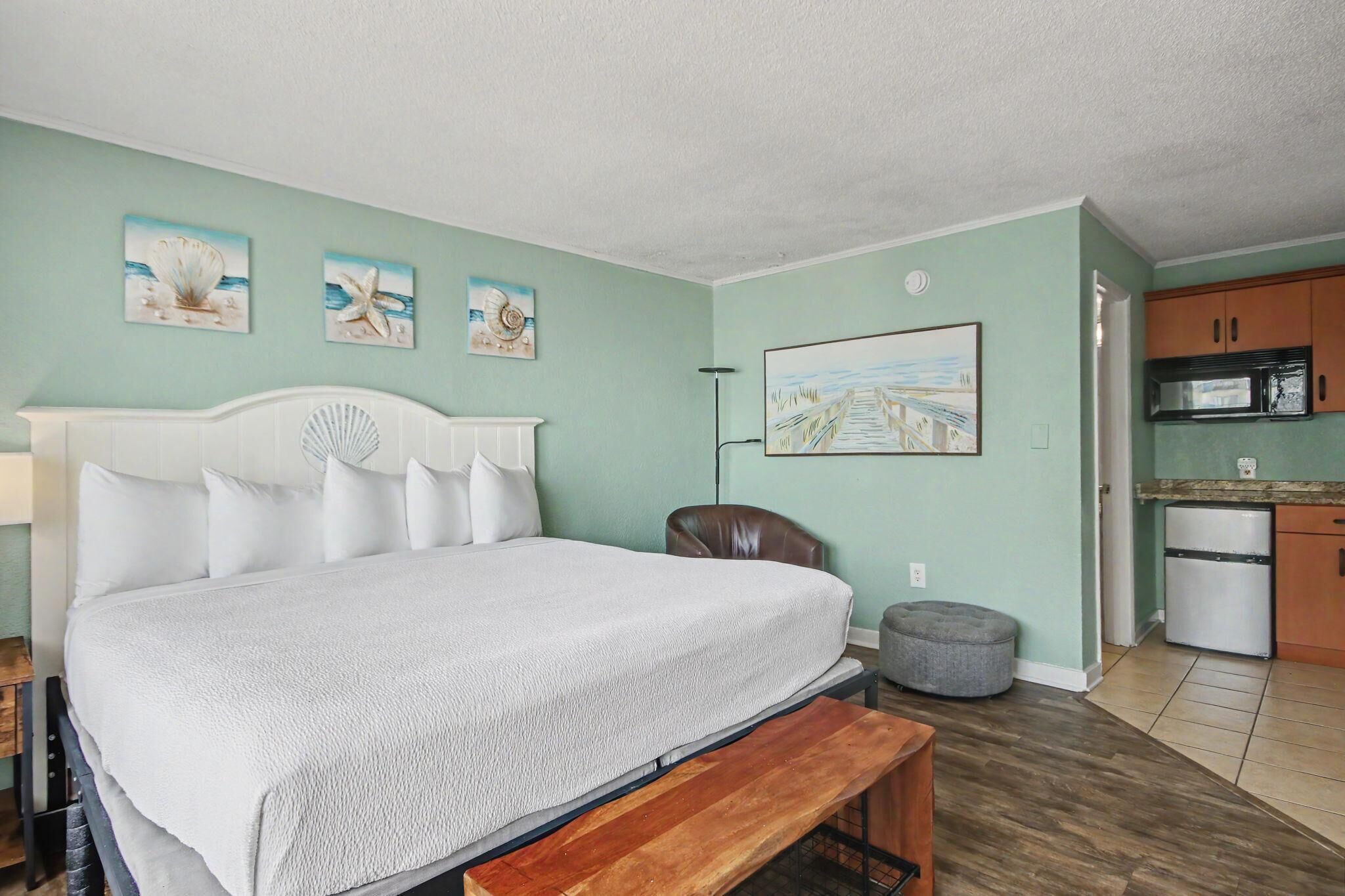 A bedroom with a bed, a bench, a chair, a small ottoman, and a painting on the wall.