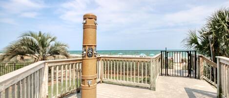 A wooden deck with a metal railing, a palm tree, and a view of the ocean.