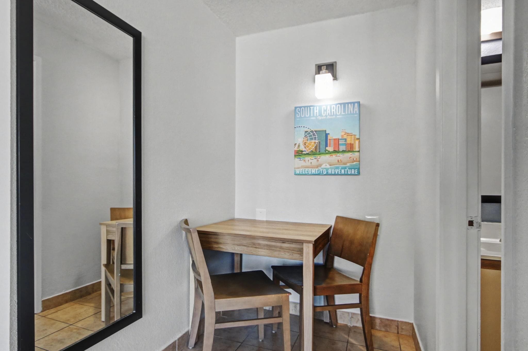 A room with a wooden table and chairs, a poster on the wall, and a mirror.