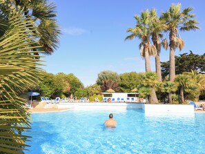 En swimmingpool med kristallklart blått vatten, omgiven av palmer och solstolar.