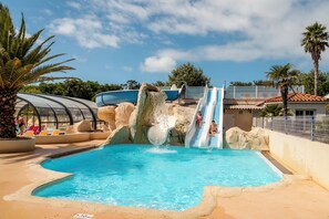 A swimming pool with a water slide, palm trees, and a clear sky. - Oléon - Confort 3 TV – 6p (1) (Saint-Georges-d'Oléron)