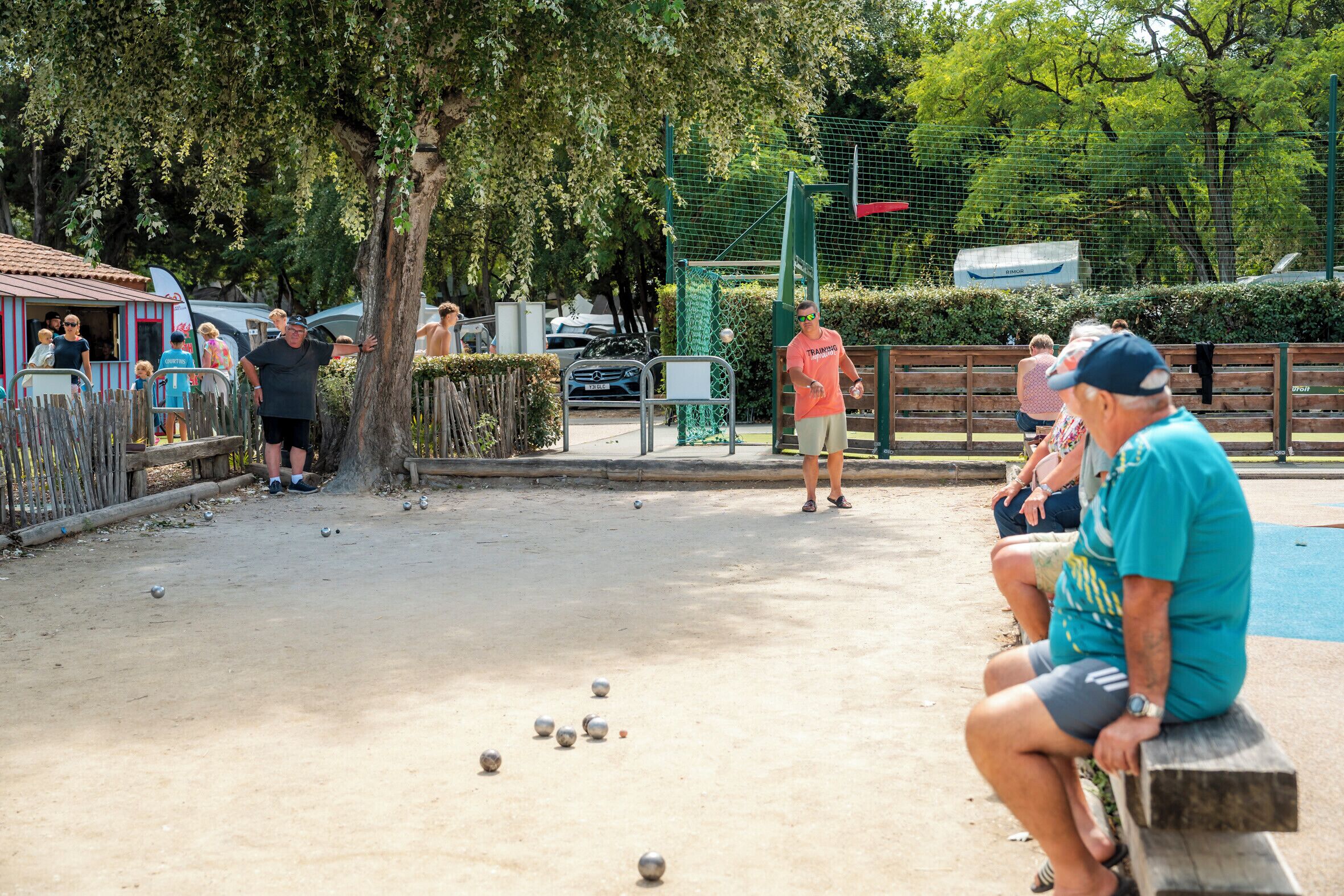 En park med boccebane, bænke og et hegn omkring træer.