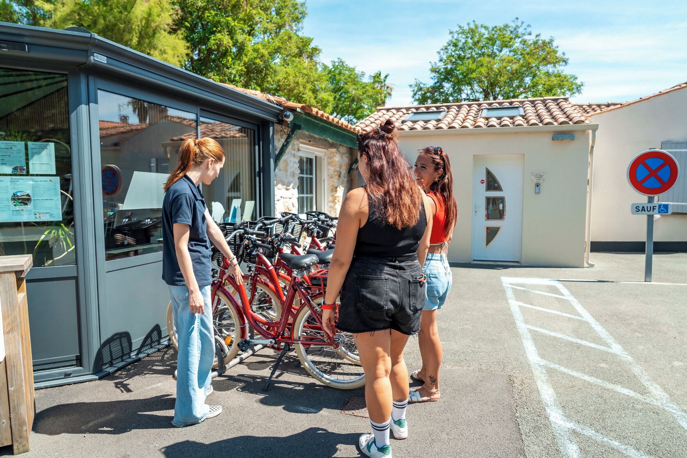 Un edificio con puerta de cristal, una bicicleta roja estacionada afuera y un letrero de prohibido estacionar.