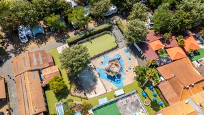 Ovenfra ses et boligområde med en legeplads, en swimmingpool og en tennisbane.