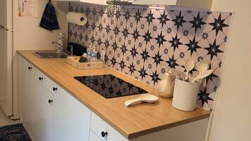 Una cocina con encimera de madera, armarios blancos, salpicadero con estampado de estrellas en blanco y negro, un lavamanos y un cubo de basura.