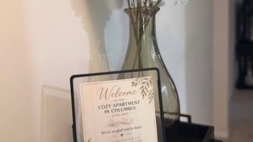 Un cartell de benvinguda amb un codi QR, un ram de flors blanques en un vas i un safata negra amb una nansa daurada.