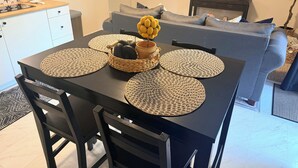 Una mesa de comedor con individuales tejidos, una cesta de frutas y un televisor al fondo.