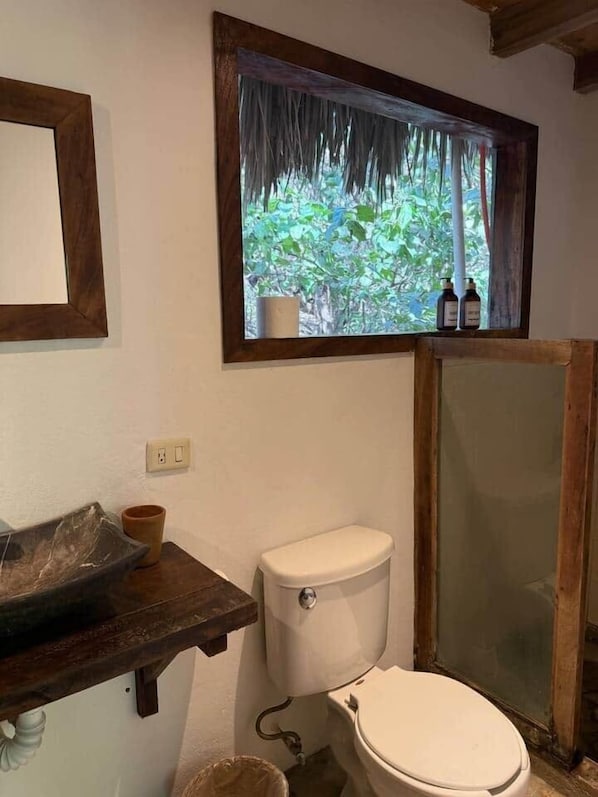 Une salle de bain équipée de toilettes, d’un lavabo et d’une fenêtre donnant sur un espace verdoyant.