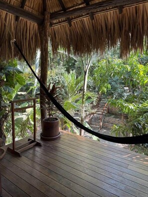 Une terrasse en bois surmontée d’un toit de chaume, entourée d’une végétation tropicale luxuriante.